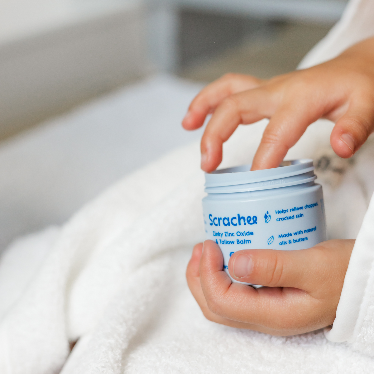 Person holding a jar of Scracher balm with a blurred background