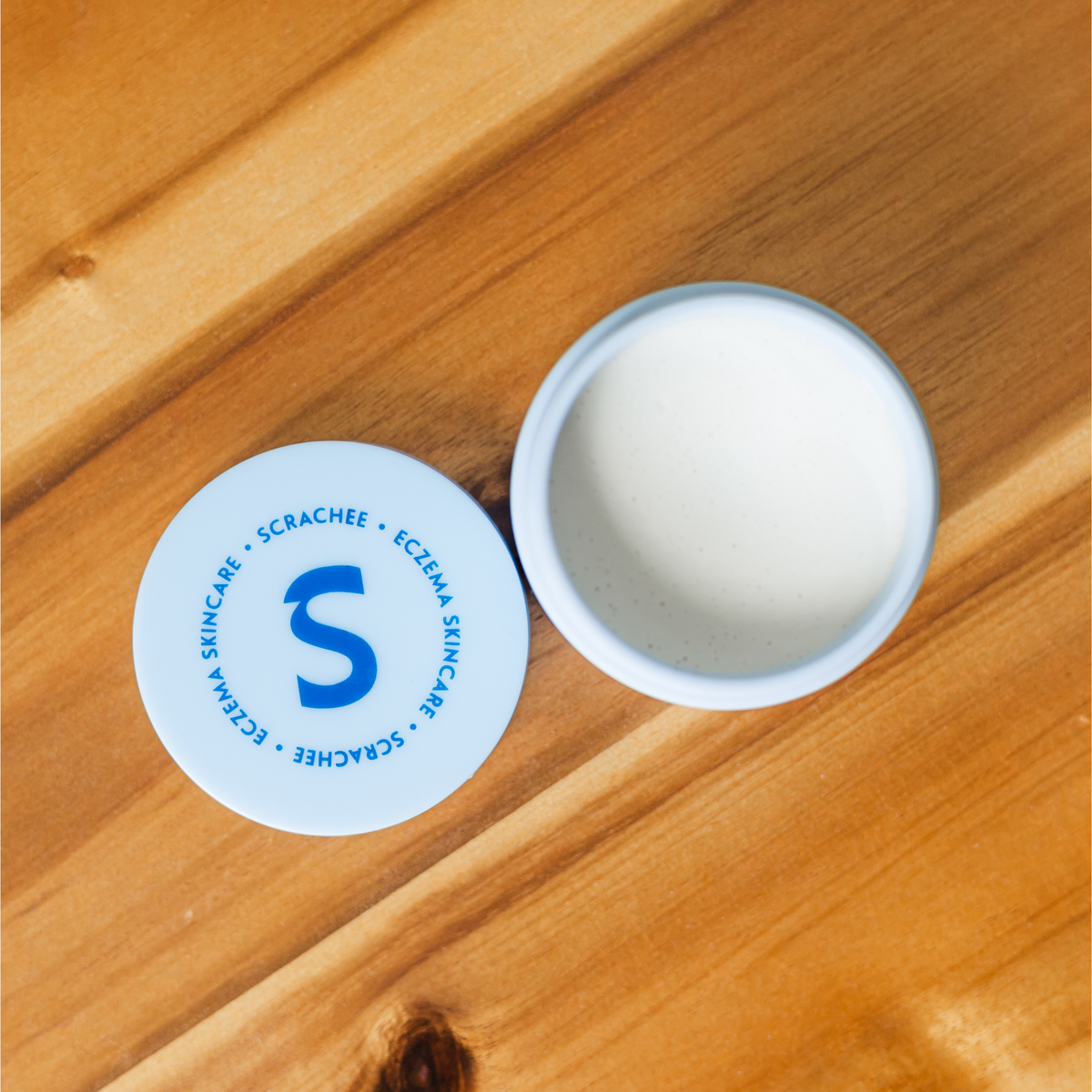 Scrachee skincare product with a circular label featuring a blue 'S' logo on a wooden surface.