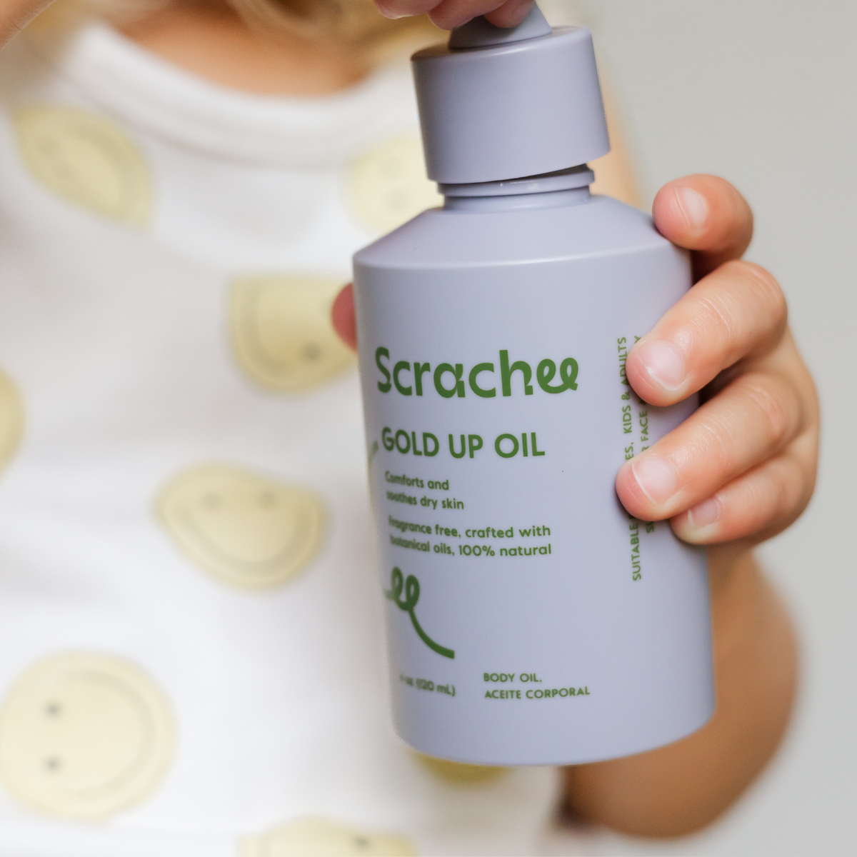 Hand holding a bottle of Scraches Gold Up Oil with a blurred background