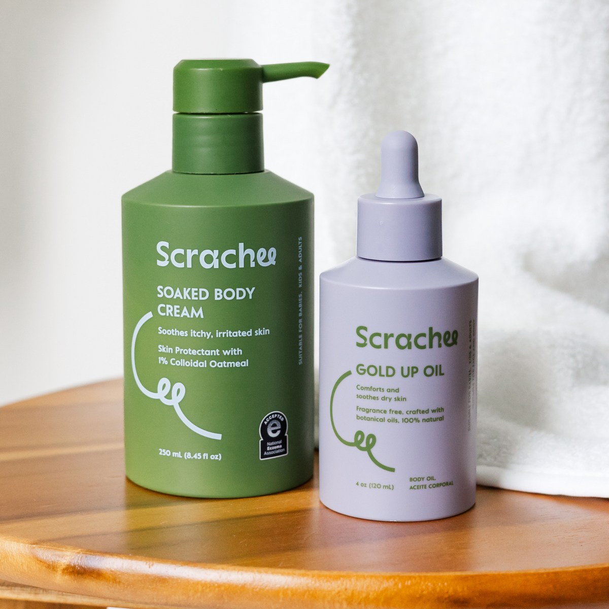 Two bottles of Scrachee products on a wooden surface with a white towel in the background.